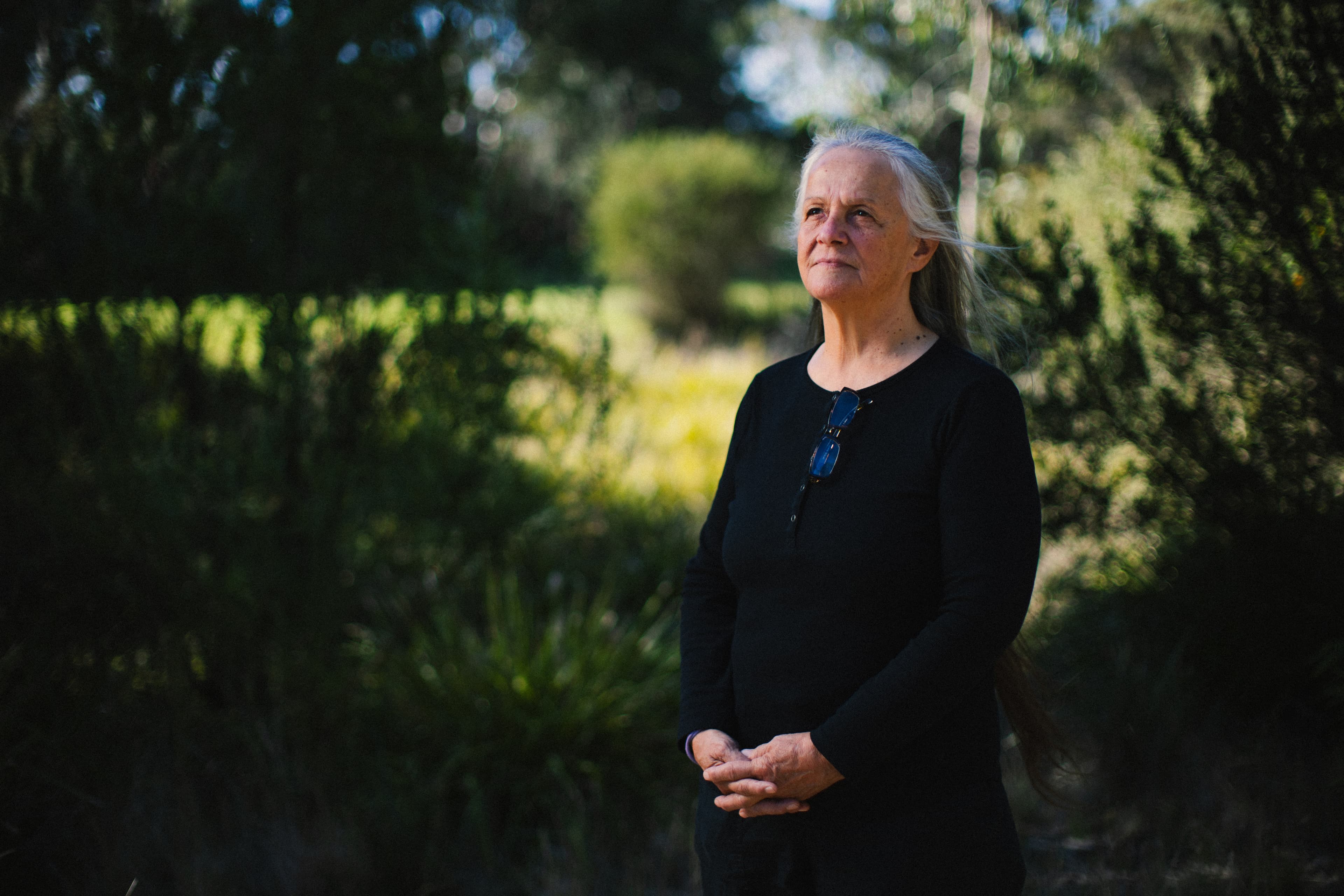 Keerray Woorroong Gunditjmara woman Dr Vicki Couzens poses in a natural setting, surrounded by softly blurred green trees.