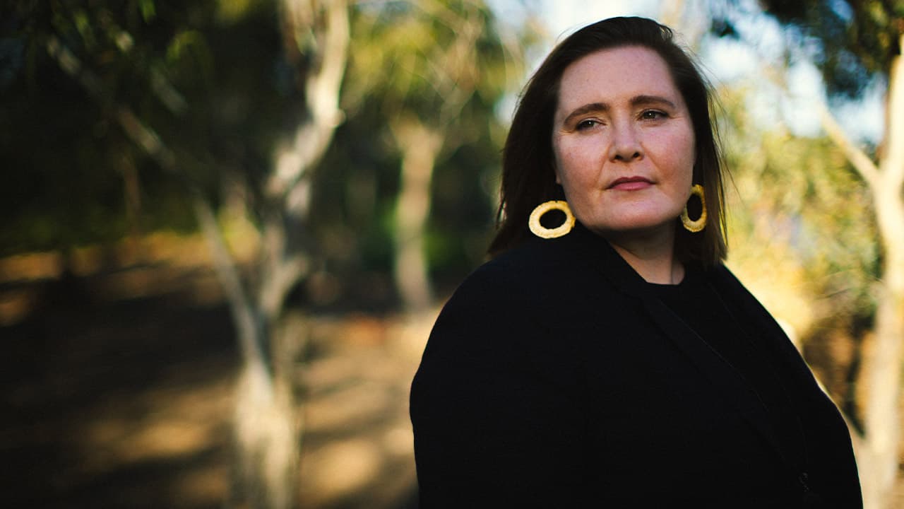 Headshot of Gomeroi woman, Dr Nikki Moodie with out of focus gum trees in the background.
